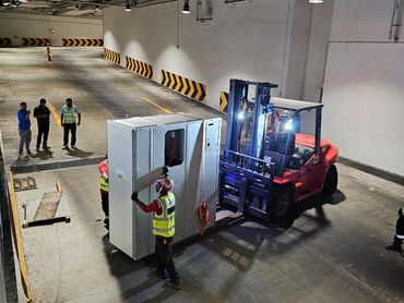 Workers using a forklift in an industrial facility to move large equipment.