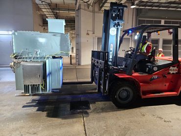 Forklift carrying industrial equipment inside a warehouse with workers.