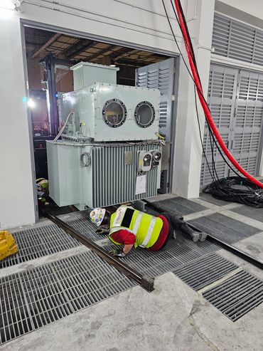 Worker inspecting electrical equipment on the floor in an industrial setting.