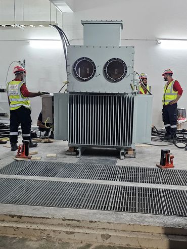 Workers in safety gear working on a large industrial transformer.