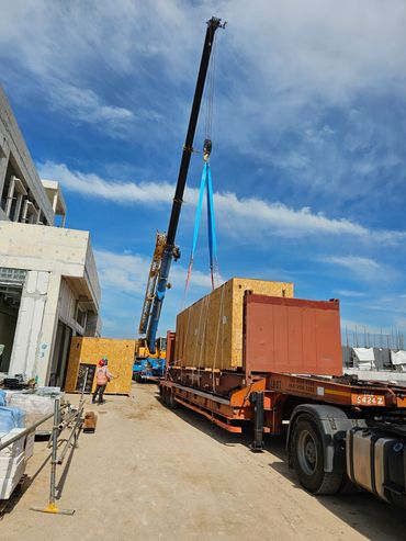 Crane lifting a large wooden crate at a construction site under a blue sky.