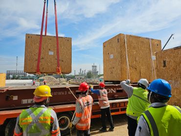 Workers in safety gear guide a large crate being lifted by a crane at a construction site.