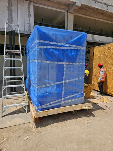 Workers unpacking large equipment wrapped in blue plastic at a construction site.