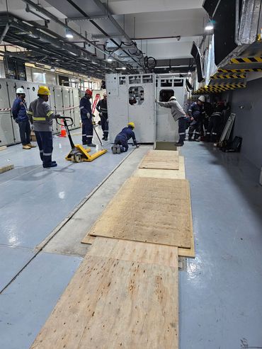 Workers in safety gear install large electrical equipment indoors.