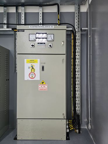 Electrical AC distribution panel with warning signs and connected cables.