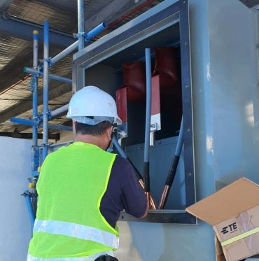 Electrician working on a large electrical panel wearing safety gear.