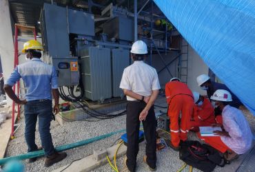 Technicians working on electrical equipment, wearing safety gear and helmets.