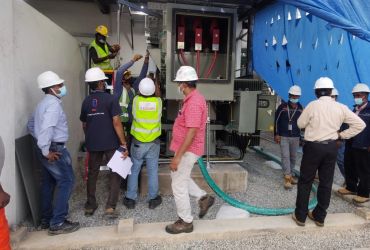Construction workers inspecting electrical equipment while wearing safety gear.