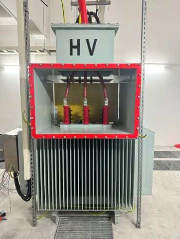 High voltage electrical transformer with red and black cables.