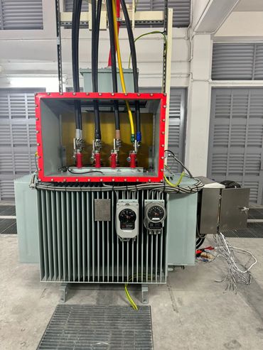 Industrial transformer with visible cables and gauges in a facility.