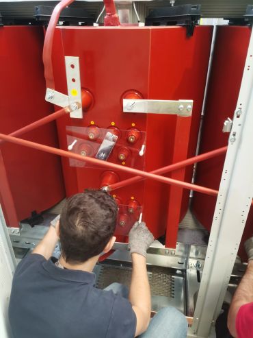 Technician working on a large red electrical transformer inside a cabinet.