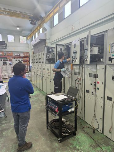 Technicians working on electrical panels in an industrial workshop.