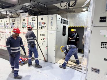 Workers in helmets installing electrical switchgear panels in an industrial setting.