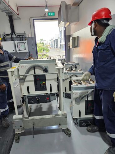 Two workers in safety gear handling electrical equipment inside a facility.
