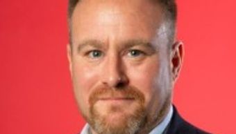 Professional headshot of a man against a red background.