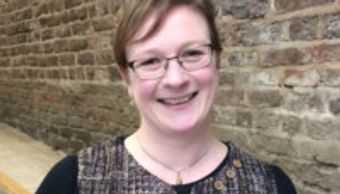 Smiling woman with glasses in front of a brick wall.