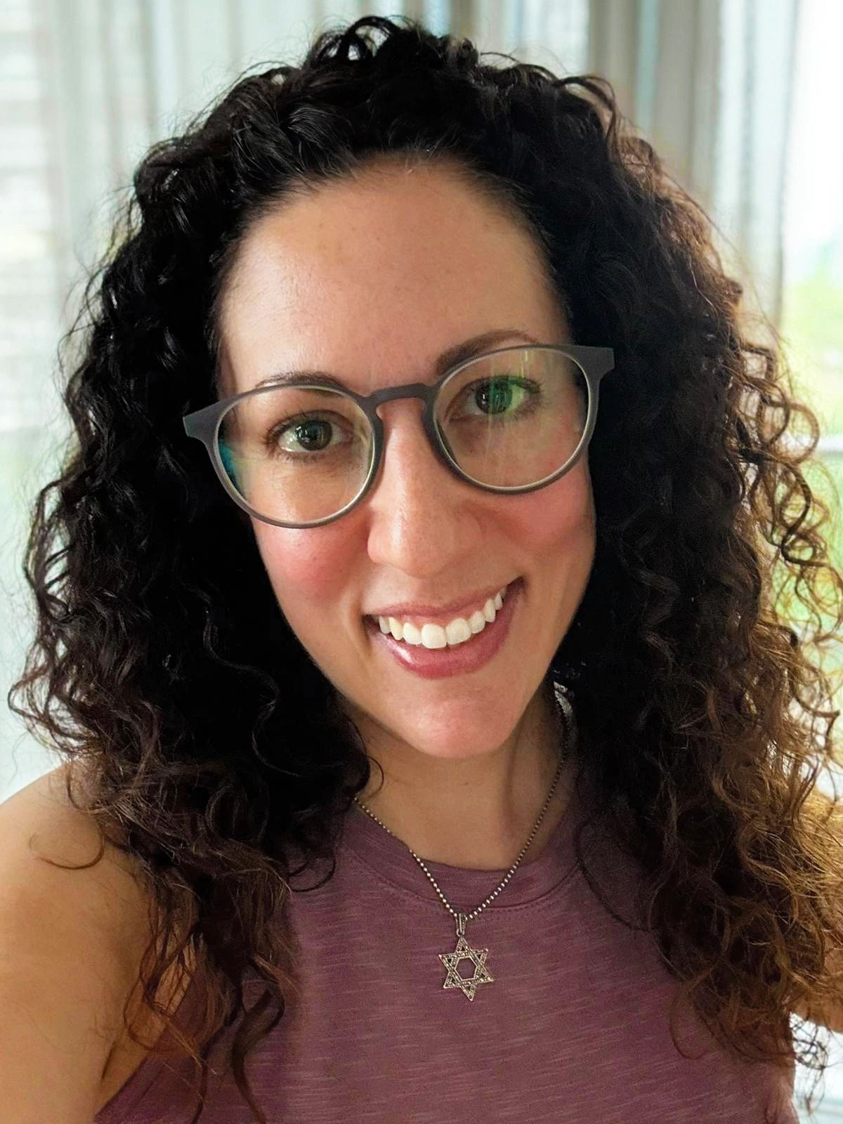 Smiling woman with curly hair, glasses, and a Star of David necklace.