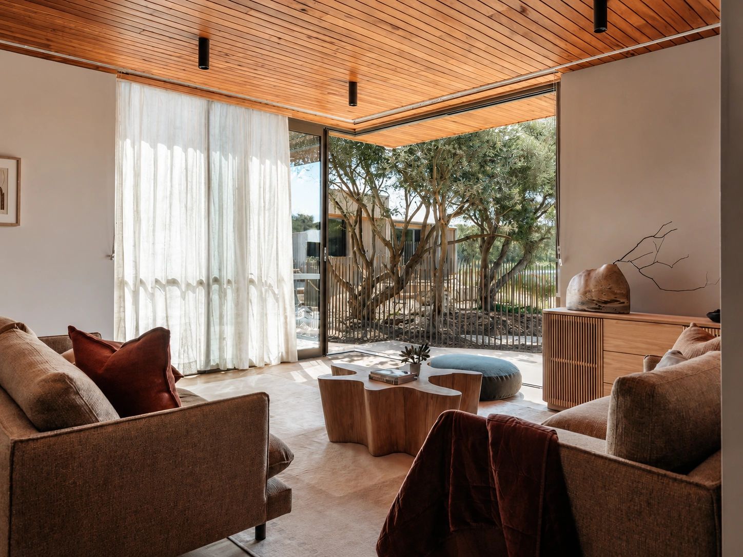 Cozy living room with wooden ceiling and large glass windows overlooking trees.