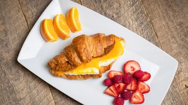 Breakfast croissant with chorizo, egg, cheese, with a side of orange slices, and strawberries.