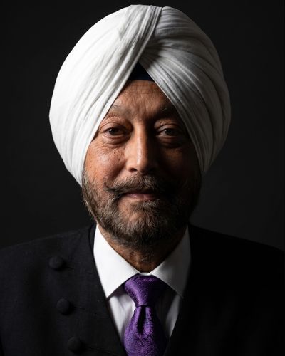 Portrait of a distinguished man wearing a white turban and purple tie against a dark background.