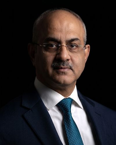 Professional portrait of a middle-aged man in glasses and suit against a black background.