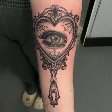 Ornate black and grey eye tattoo inside heart-shaped mirror