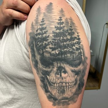 Black and grey skull tattoo with pine forest landscape by Eric at Steel Rod Tattoo