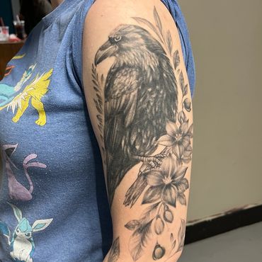 Black and grey raven and floral tattoo on upper arm
