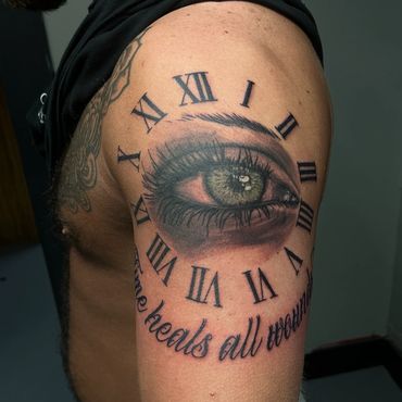 Realistic eye tattoo surrounded by Roman numerals on upper arm