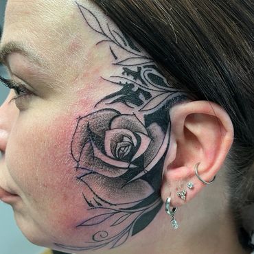 Black and grey rose face tattoo extending from cheek to temple