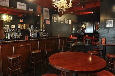 Cozy bar interior with wooden stools and tables under chandeliers.