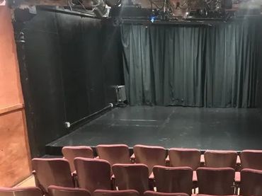 Small theater with rows of seats facing a black stage and curtain.
