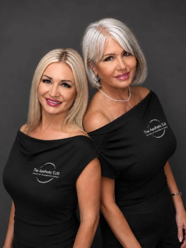 Two women in matching black dresses smiling.