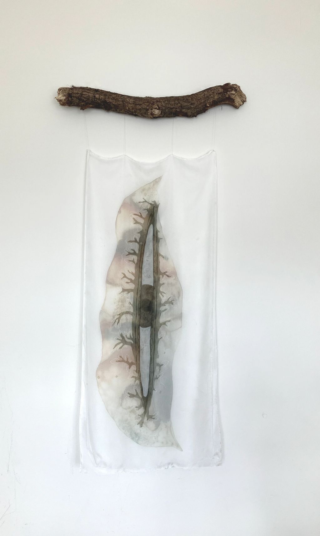 Hanging fabric art with organic design on a rustic wooden branch.
