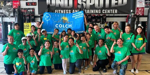 Group of diverse kids and adults in green shirts posing at a fitness center.