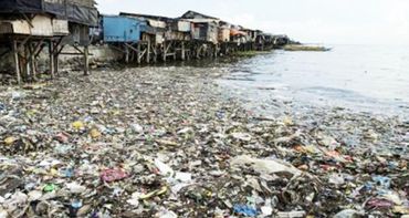 Coastal area heavily polluted with plastic waste near stilt houses.