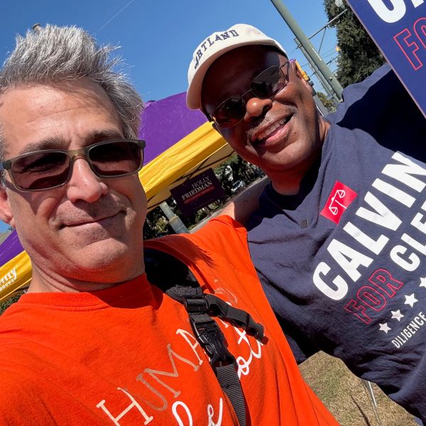Two men smiling outdoors at a public event.