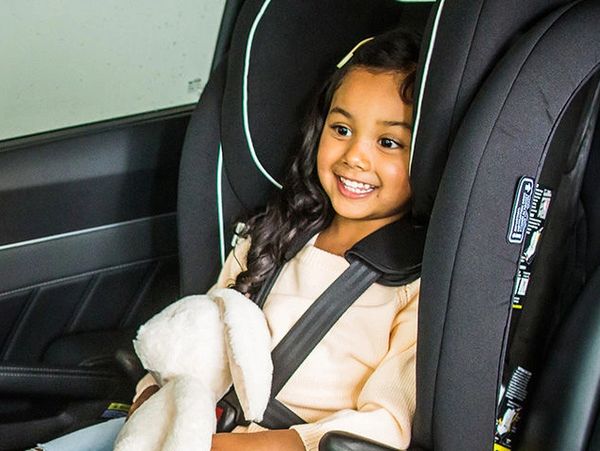 Smiling girl secured in a car seat holding a plush toy.
