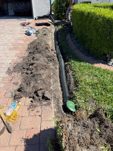 Drainage pipe being installed beside a curved paver walkway and hedge.