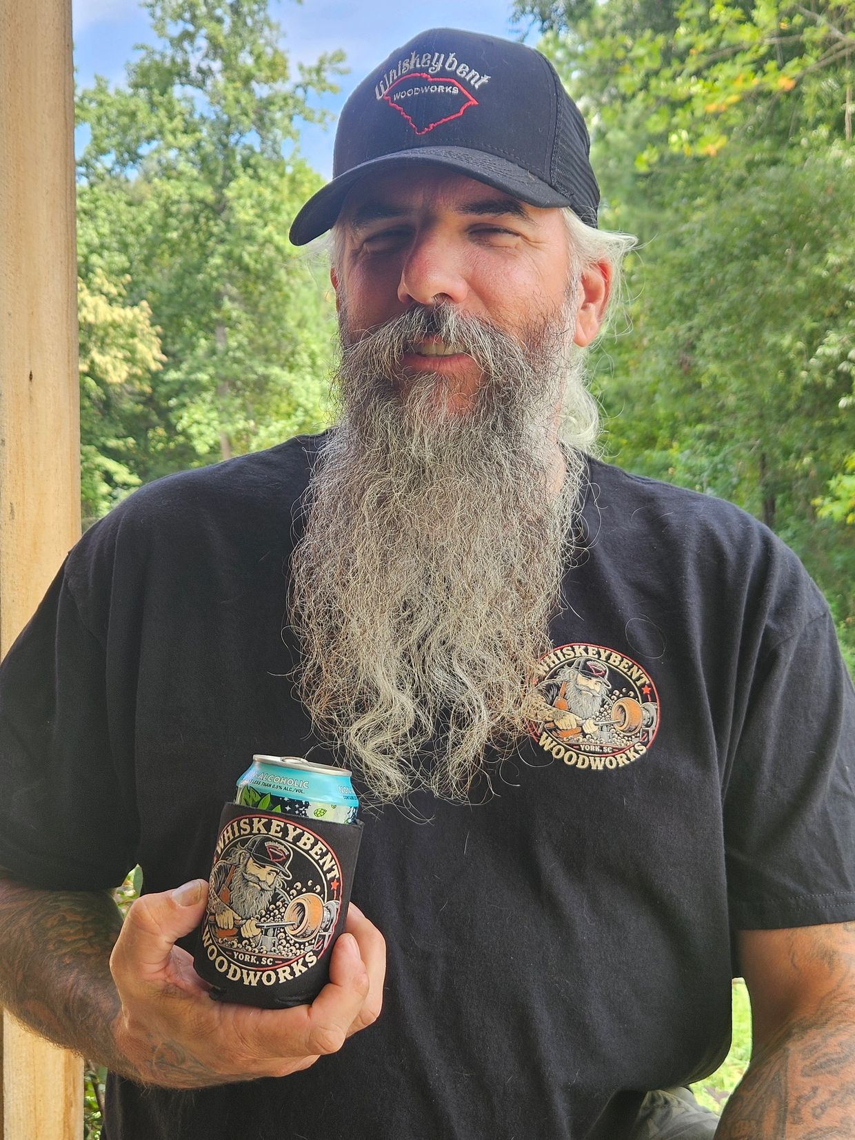 Man with a long beard holding a drink can outdoors.