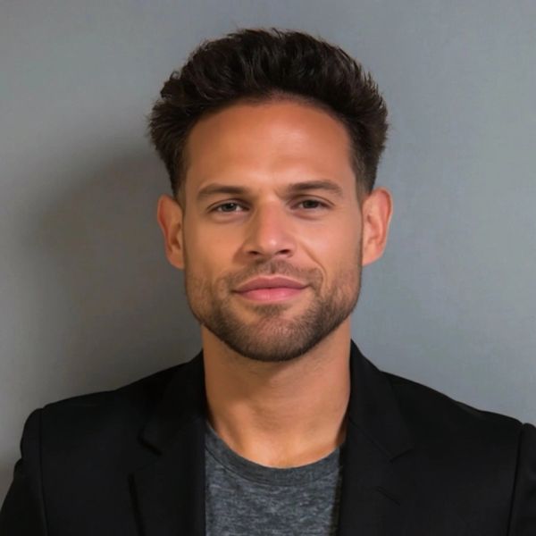 Confident man with styled hair wearing a black blazer and gray shirt.