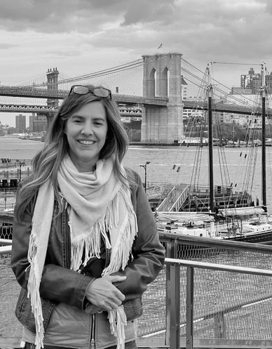 A woman smiles near a waterfront with the Brooklyn Bridge in the background.