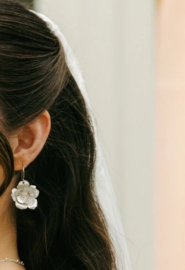 A woman with dark hair and floral earrings posing gracefully outdoors.