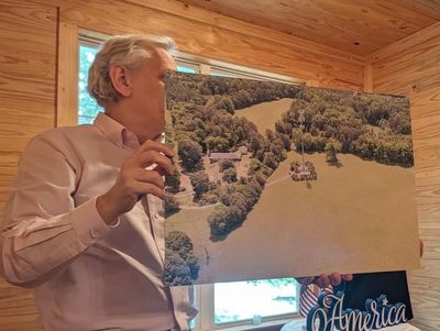 Man holding an aerial photo of a landscape inside a wooden room.