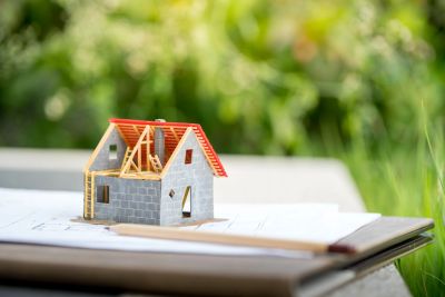 A miniature house model on architectural blueprints outdoors.