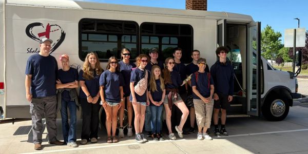 Group of young people standing in front of a white bus.