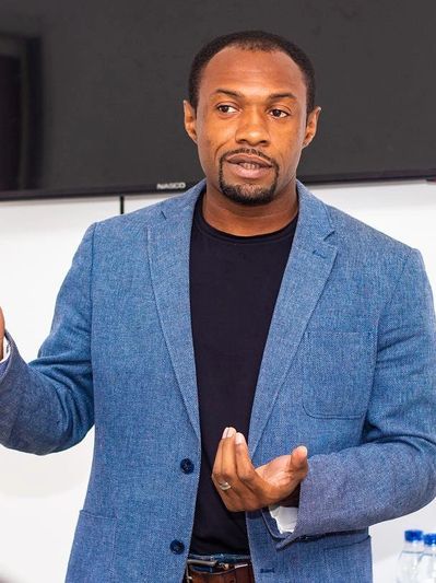 Man in blue blazer giving a presentation or speech indoors.