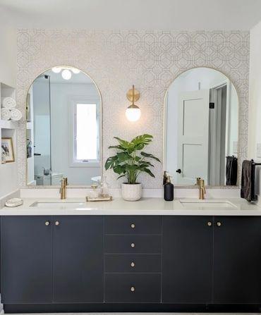 Modern bathroom renovation. Vanity with dual arched mirrors, dark blue cabinetry and gold accents.