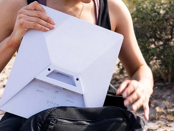 Person placing a white device into a black bag outdoors.