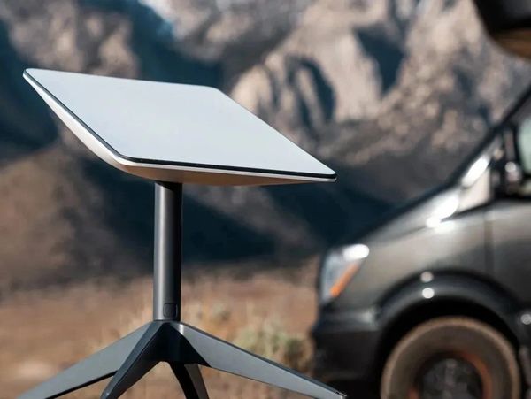A modern, sleek outdoor table with a tilted surface and tripod base, set against a mountainous backdrop.